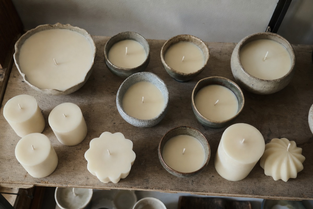 Velas recién vertidas solidificándose en un estante del taller durante la espera