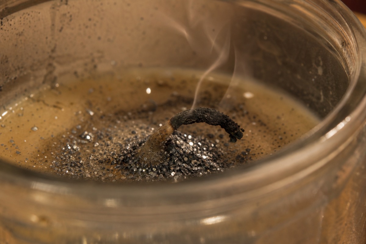 Mecha carbonizada y doblada, recubierta de purpurina plateada acumulada en la cera solidificada; la vela está apagada.