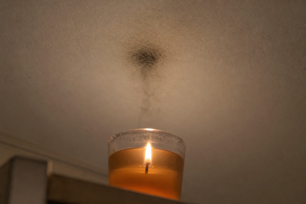 Mancha oscura de hollín en un techo blanco, justo encima de una vela de gel encendida en un vaso de vidrio